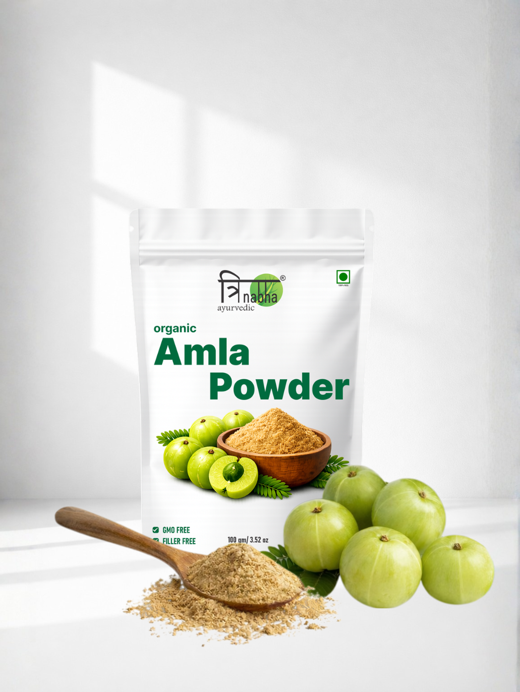 A wooden spoon with organic Amla powder next to fresh green Indian Gooseberries and the Trinabha product pouch.